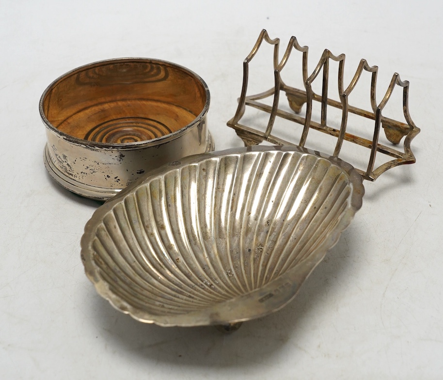 A George VI silver shell dish, Sheffield, 1946, 14.2cm, a modern silver mounted wine coaster and a late Victorian silver five bar toast rack. Condition - fair
